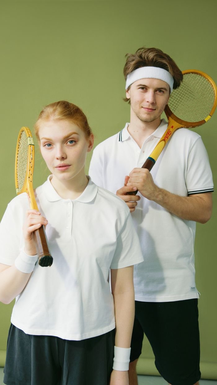 Young male and female squash players posing with rackets against a green background.